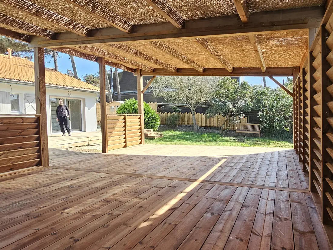 Terrasse bois couverte, fermée par un claustra, ouvrant sur une pelouse
