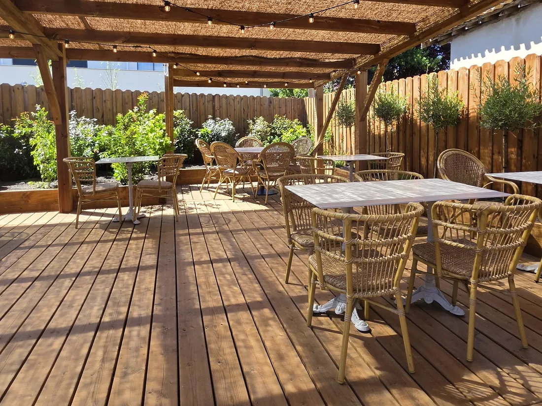 Terrasse sous pergola couverte de canisse, plancher bois et tables dressées